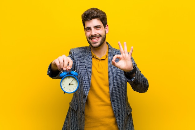 Jeune bel homme avec un réveil sur fond orange