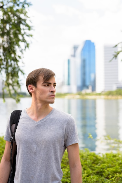 Jeune bel homme avec sac à dos relaxant dans le parc