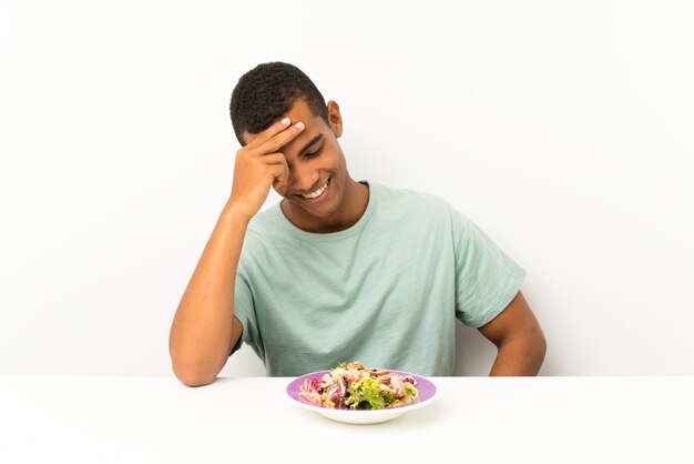 Jeune bel homme avec une salade dans une table en riant