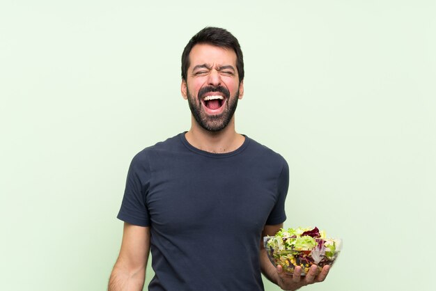 Jeune bel homme avec une salade sur un mur vert isolé, criant à l'avant avec la bouche grande ouverte