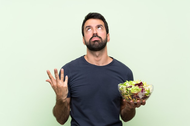 Jeune bel homme avec salade sur mur vert isolé frustré par une mauvaise situation