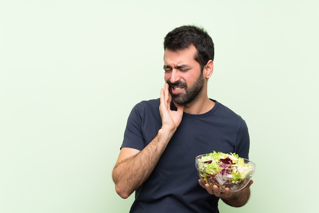 Jeune bel homme avec salade sur mur vert isolé avec maux de dents