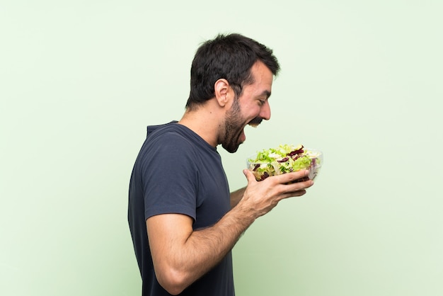 Jeune bel homme avec une salade sur un mur vert isolé