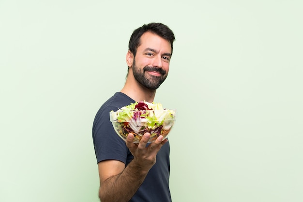 Jeune bel homme avec une salade sur un mur vert isolé