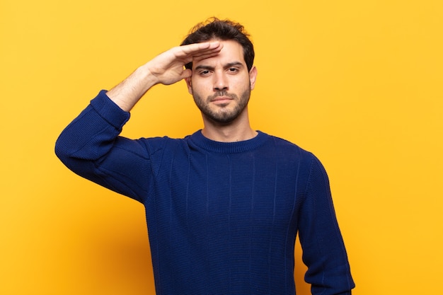 Jeune bel homme saluant la caméra avec un salut militaire dans un acte d'honneur et de patriotisme, montrant du respect