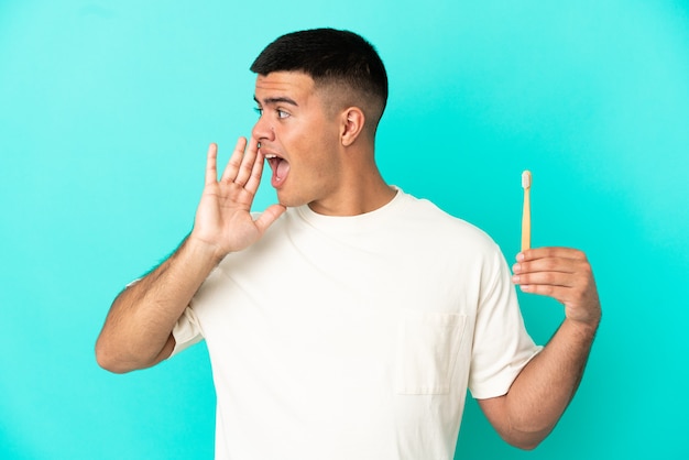 Jeune bel homme se brosser les dents sur fond bleu isolé en criant avec la bouche grande ouverte sur le côté