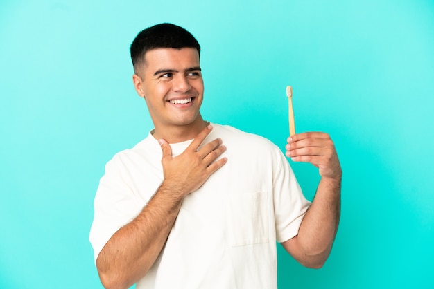 Jeune bel homme se brosser les dents sur fond bleu isolé en levant tout en souriant