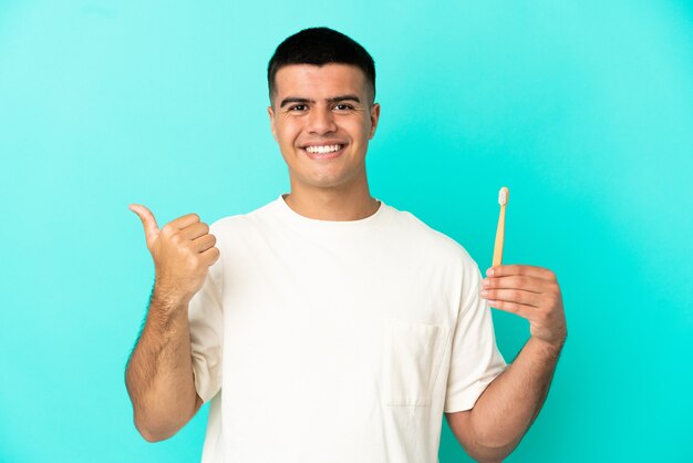 Jeune bel homme se brosser les dents sur fond bleu isolé pointant sur le côté pour présenter un produit