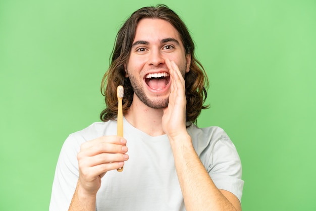 Jeune bel homme se brosser les dents sur fond isolé criant avec la bouche grande ouverte