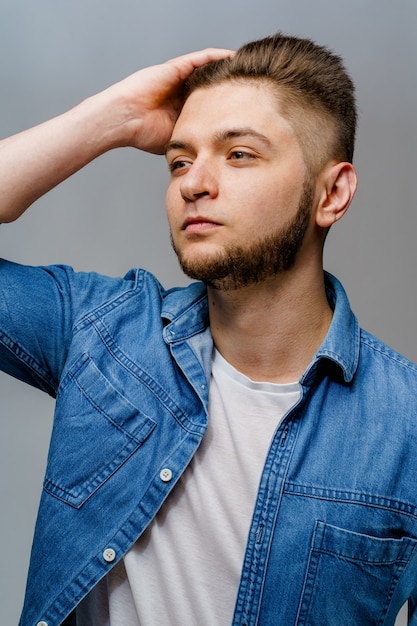 Jeune bel homme se dresse sur une surface blanche et touche ses cheveux après avoir visité le salon de coiffure