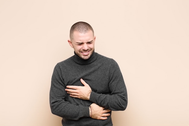 Jeune bel homme se sentant anxieux, malade, malade et malheureux, souffrant de maux d'estomac douloureux ou de grippe contre un mur plat