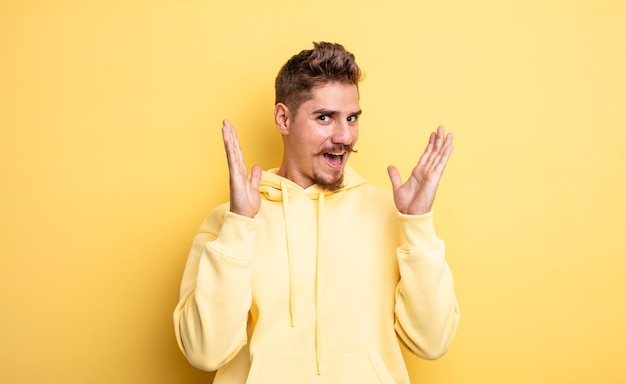 Jeune bel homme se sentant choqué et excité, riant, étonné et heureux à cause d'une surprise inattendue. concept de moustache étrange