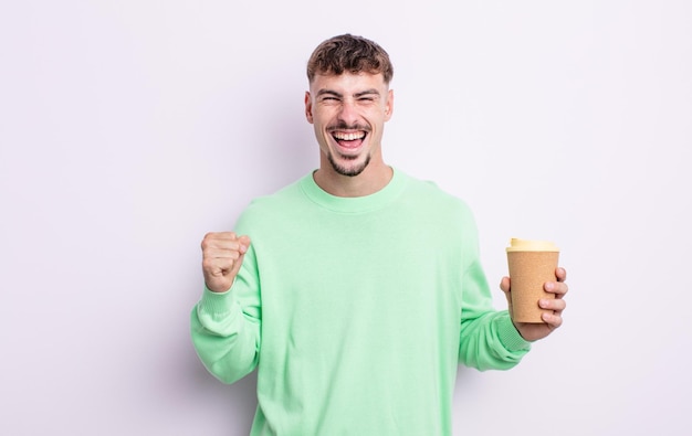 Jeune bel homme se sentant choqué, riant et célébrant le succès. concept de café à emporter