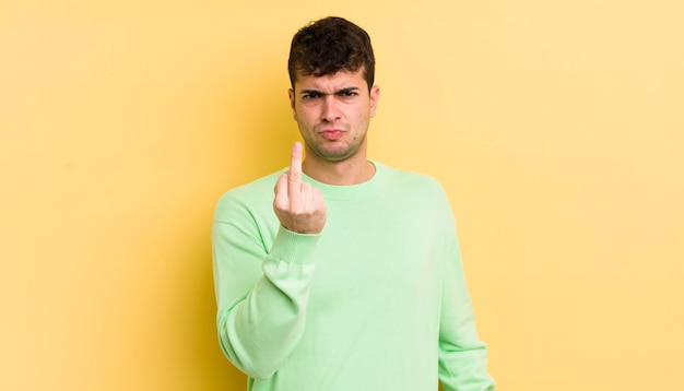 Jeune bel homme se sentant en colère agacé rebelle et agressif renversant le doigt du milieu ripostant