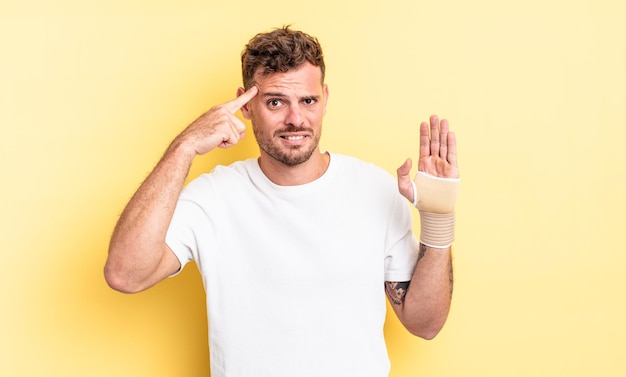 Jeune bel homme se sentant confus et perplexe, montrant que vous êtes fou. concept de bandage à la main