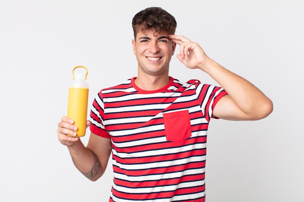 Jeune bel homme se sentant confus et perplexe, vous montrant que vous êtes fou et tenant un thermos à café