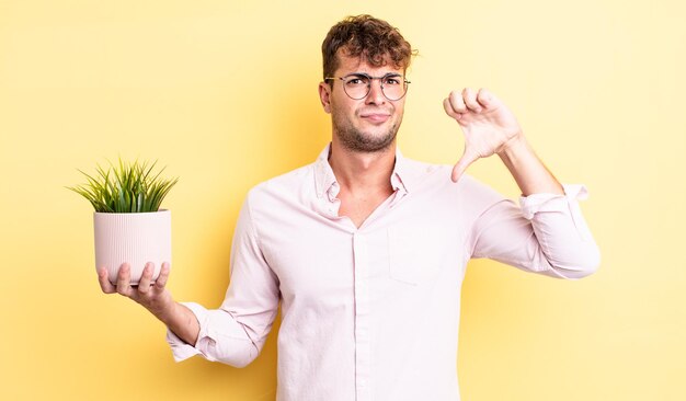 Jeune bel homme se sentant croisé, montrant les pouces vers le bas. concept de plante décorative