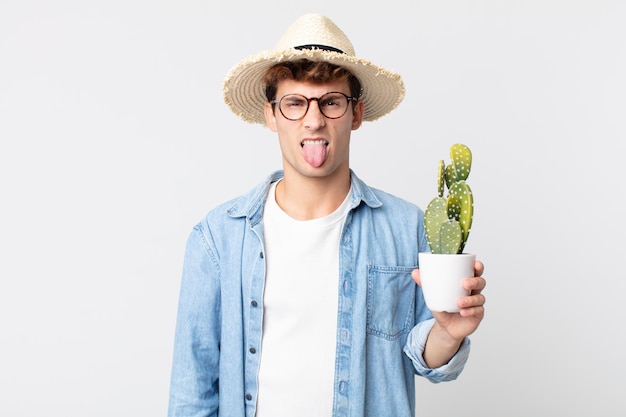 Jeune bel homme se sentant dégoûté et irrité et tirer la langue. agriculteur tenant un cactus décoratif