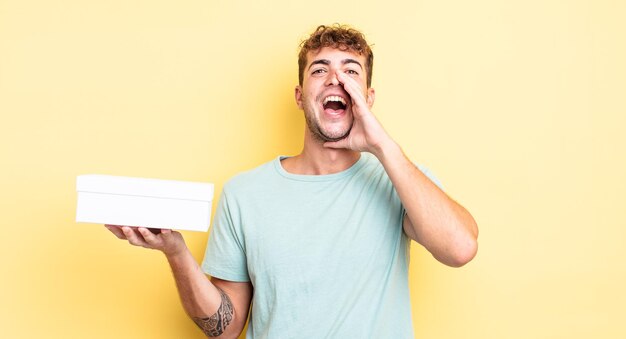 Jeune bel homme se sentant heureux, donnant un grand cri avec les mains à côté de la bouche. concept de boîte blanche