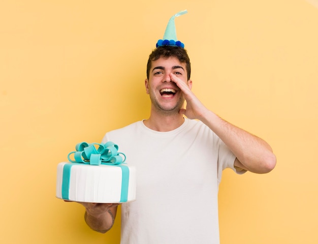 Jeune bel homme se sentant heureux en donnant un grand cri avec les mains à côté du concept d'anniversaire de la bouche