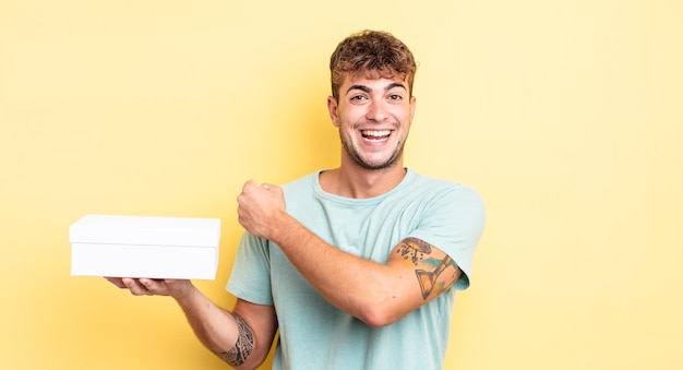 Jeune bel homme se sentant heureux et faisant face à un défi ou célébrant le concept de boîte blanche