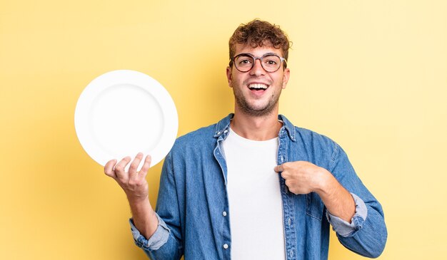 Jeune bel homme se sentant heureux et pointant vers lui-même avec un excité. concept de plat vide