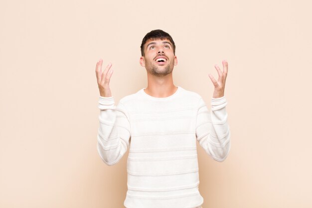 Jeune bel homme se sentir heureux, étonné, chanceux et surpris, célébrant la victoire avec les deux mains en l'air contre un mur chaud