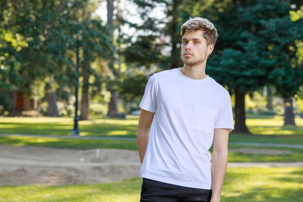 Un jeune bel homme se tient au parc et regarde au loin