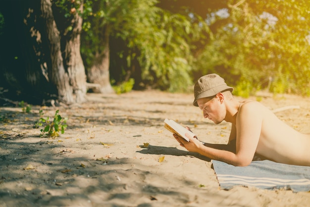 Jeune bel homme séduisant au Panama allongé sur la plage de sable paradisiaque et la lecture d'un livre sur une journée d'été