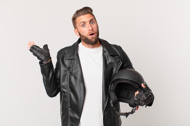 Jeune bel homme semblant surpris et choqué, avec la mâchoire baissée tenant un objet. concept de casque de moto