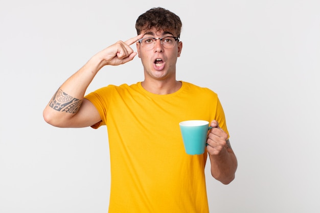 Jeune bel homme semblant surpris, réalisant une nouvelle pensée, idée ou concept et tenant une tasse de café