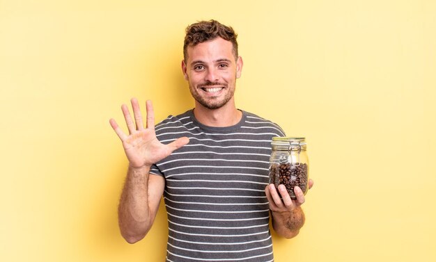 Jeune bel homme souriant et à l'air sympathique, montrant le concept de grains de café numéro cinq