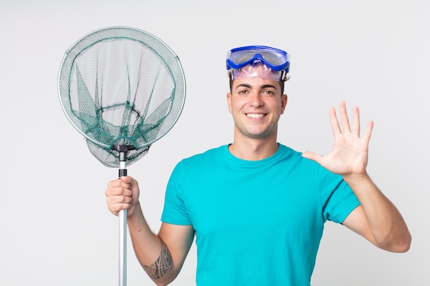 jeune bel homme souriant et à l'air sympathique, montrant le numéro cinq avec des lunettes et un filet de pêche