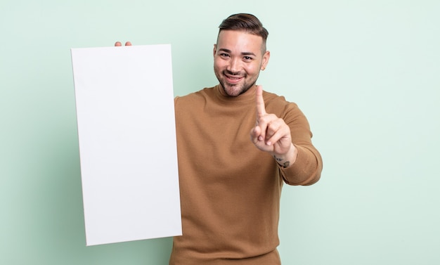 Jeune bel homme souriant et à l'air sympathique, montrant le numéro un. concept de toile vide