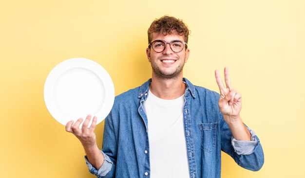 Jeune bel homme souriant et à l'air sympathique, montrant le numéro deux. concept de plat vide