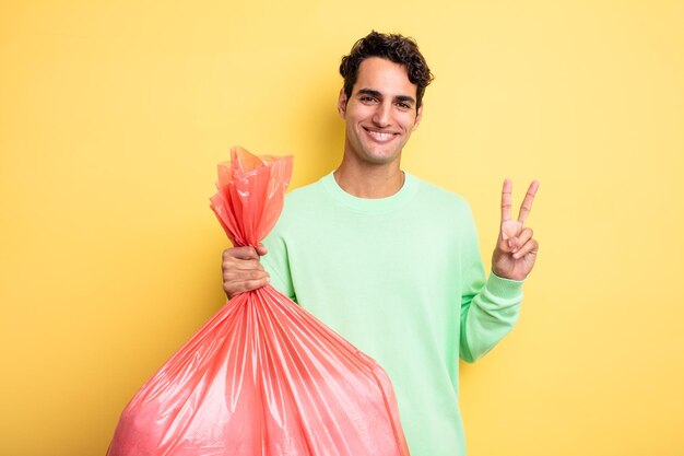 Jeune bel homme souriant et à l'air sympathique, montrant le numéro deux. concept de sac poubelle