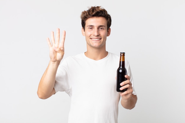 Jeune bel homme souriant et à l'air sympathique, montrant le numéro quatre et tenant une bouteille de bière