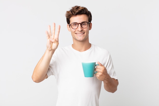 Jeune bel homme souriant et à l'air sympathique, montrant le numéro quatre et tenant une tasse de café