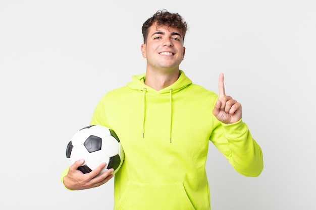 jeune bel homme souriant et à l'air sympathique, montrant le numéro un et tenant un ballon de football