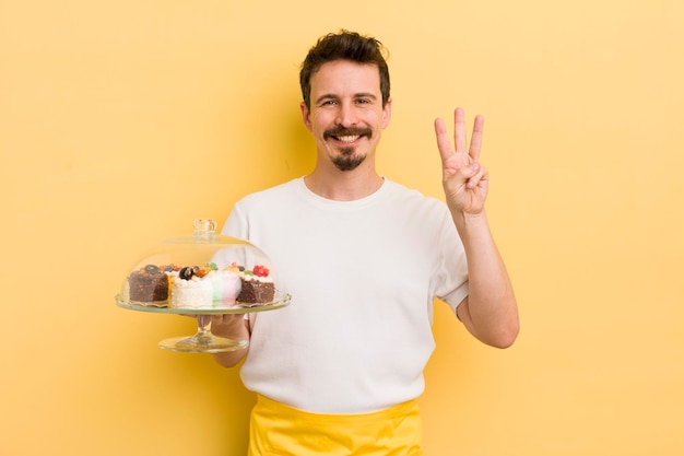 Jeune bel homme souriant et amical montrant le concept de gâteaux faits maison numéro trois