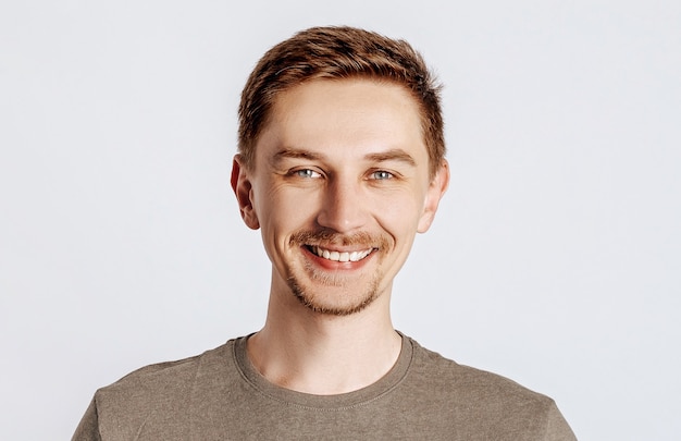 Jeune bel homme souriant avec une barbe brune. Étudiant, travailleur, homme d'affaires posant pour photo isolé sur fond gris. Place pour la publicité.