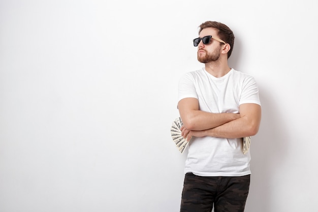 Jeune bel homme souriant avec une barbe dans une chemise blanche tenant beaucoup de billets de cent dollars. de l'argent