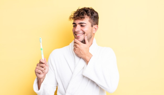 jeune bel homme souriant avec une expression heureuse et confiante avec la main sur le menton. concept de brosse à dents