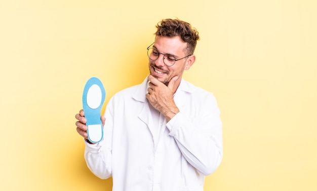 Jeune bel homme souriant avec une expression heureuse et confiante avec la main sur le menton. concept de podologue