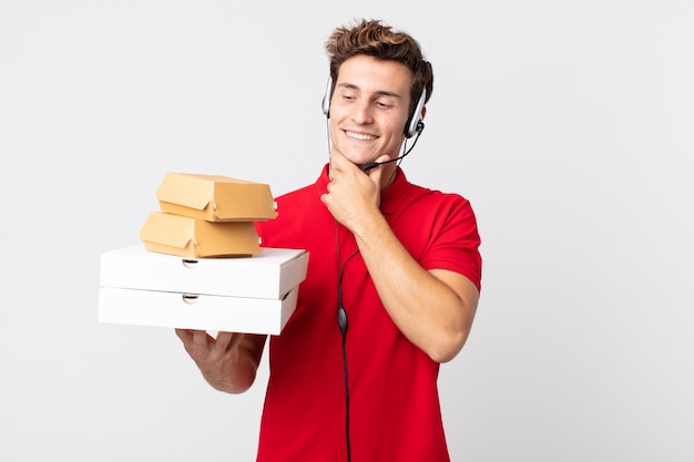 Jeune bel homme souriant avec une expression heureuse et confiante avec la main sur le menton. concept de restauration rapide à emporter