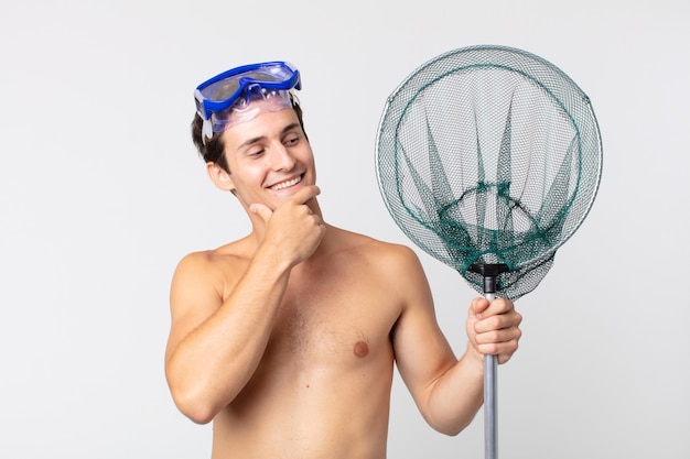 Jeune bel homme souriant avec une expression heureuse et confiante avec la main sur le menton avec des lunettes et un filet de pêche