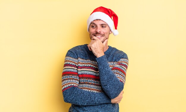 Jeune bel homme souriant avec une expression heureuse et confiante avec la main sur le menton. notion de noël