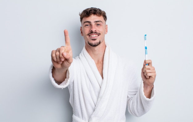 Jeune bel homme souriant fièrement et avec confiance faisant le numéro un. concept de brosse à dents