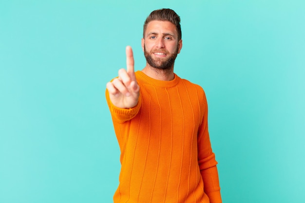 Jeune bel homme souriant fièrement et avec confiance faisant le numéro un