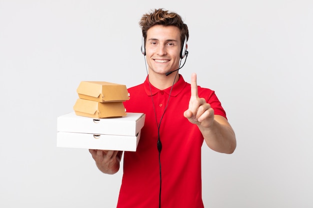 Jeune bel homme souriant fièrement et en toute confiance faisant numéro un. concept de restauration rapide à emporter